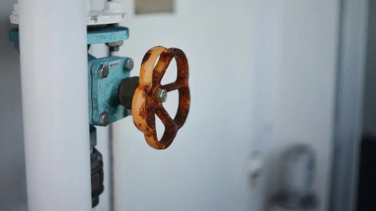 An orange rusty valve wheel on a teal water valve beside a white pipe - Leak Detection in Blandford