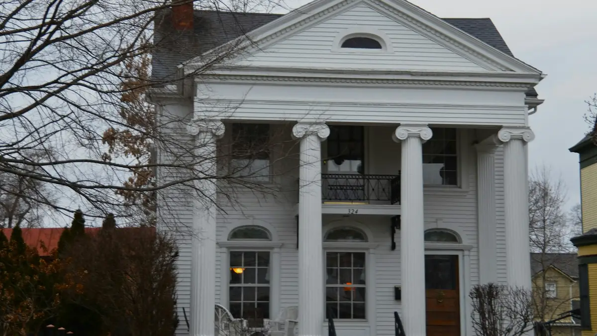 A white Greek Revival house with tall columns and a second-floor balcony behind bare trees - Leak Detection in Centre Hill