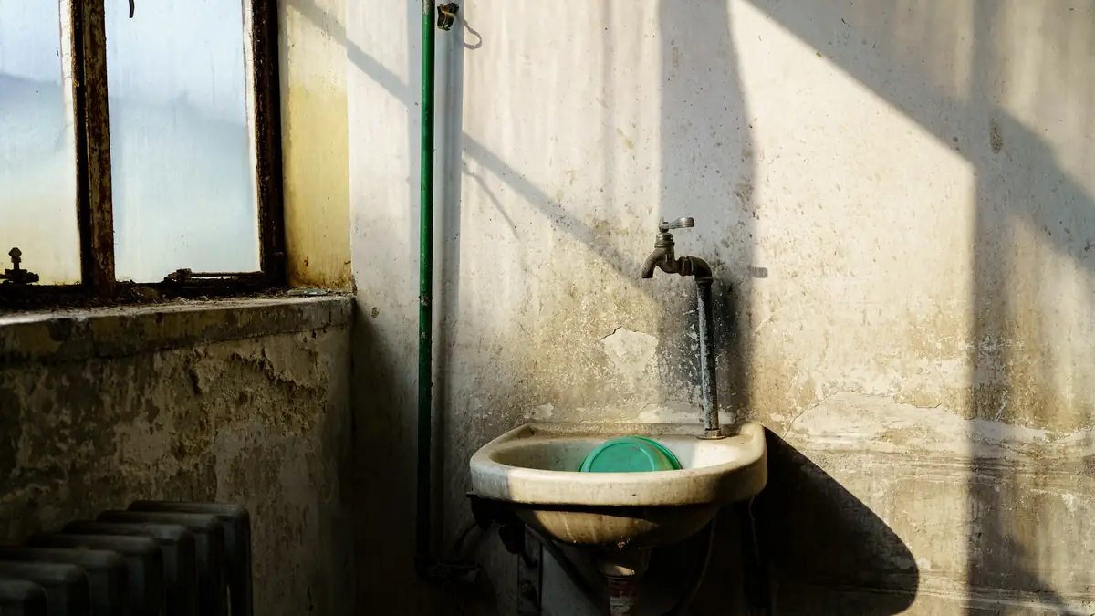 An old wall-mounted sink and tap in a sunlit utility room