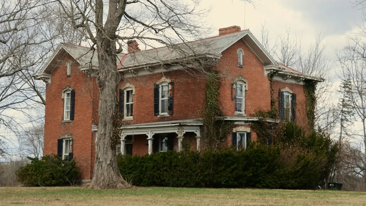 An old red brick house with a porch behind a bare oak and a clipped hedge - Leak Detection in Petersburg